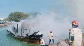 Petugas Damkar menyemprotkan air untuk mendinginkan rerangka kapal yang masih membara dan mencegah api berkobar kembali, Kamis 4 September 2025. (Foto: Lombomini.com).