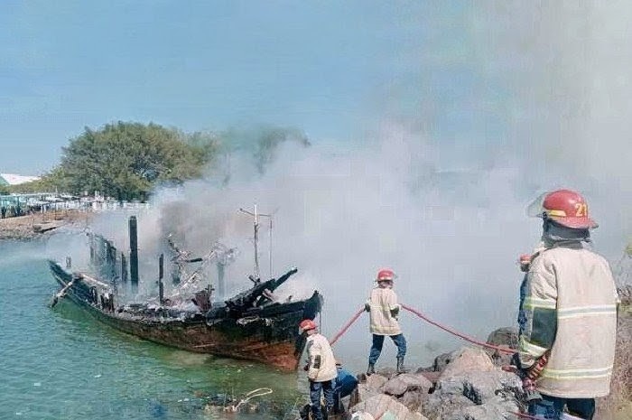 Petugas Damkar menyemprotkan air untuk mendinginkan rerangka kapal yang masih membara dan mencegah api berkobar kembali, Kamis 4 September 2025. (Foto: Lombomini.com).