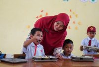 Seorang guru membagikan makanan Program Makan Bergizi Gratis (MBG) kepada siswa di salah satu sekolah. (Foto: Lombokini.com/Badan Gizi Nasional).